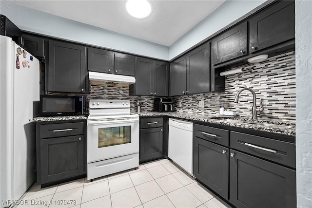 kitchen featuring white appliances, dark stone countertops, a sink, under cabinet range hood, and tasteful backsplash