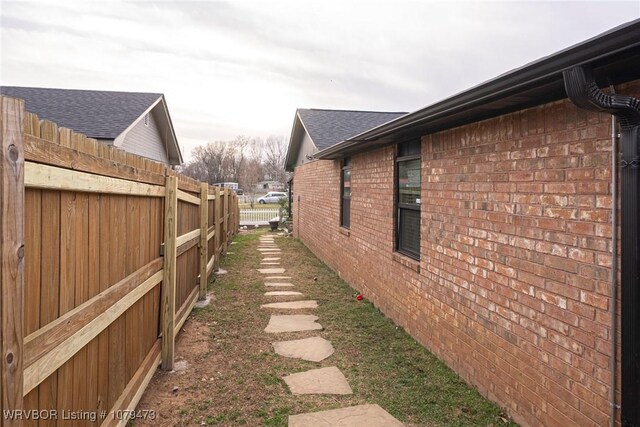 view of property exterior featuring brick siding, roof with shingles, and fence