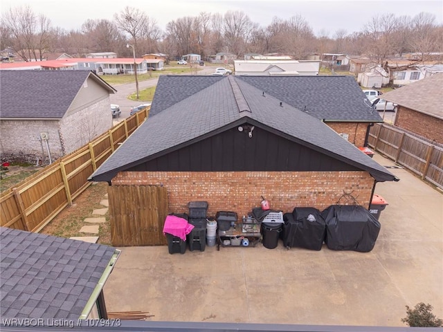 back of house featuring brick siding, a residential view, a fenced backyard, and roof with shingles