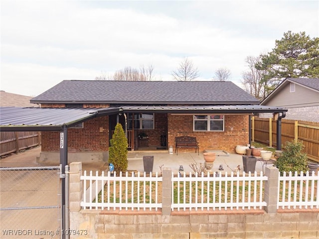 view of front of property with brick siding, a fenced front yard, roof with shingles, metal roof, and a patio area