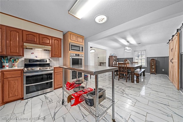 kitchen featuring a textured ceiling, stainless steel appliances, a barn door, and tasteful backsplash