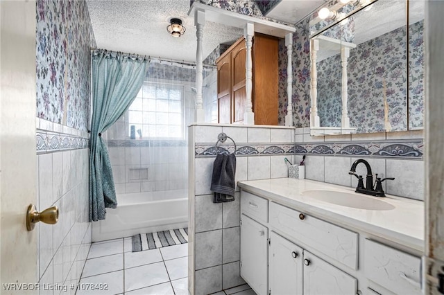 bathroom with a textured ceiling, tiled shower / bath combo, tile patterned flooring, vanity, and tile walls