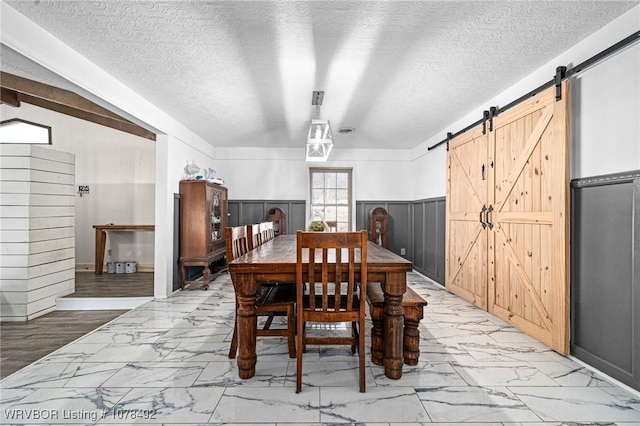 dining space with a textured ceiling, a barn door, and wooden walls