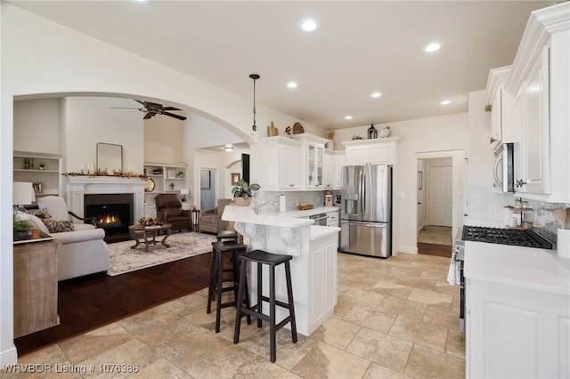 kitchen with kitchen peninsula, stainless steel appliances, ceiling fan, white cabinets, and a breakfast bar area