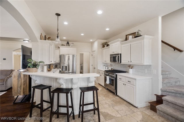 kitchen with decorative backsplash, a breakfast bar, stainless steel appliances, white cabinets, and hanging light fixtures