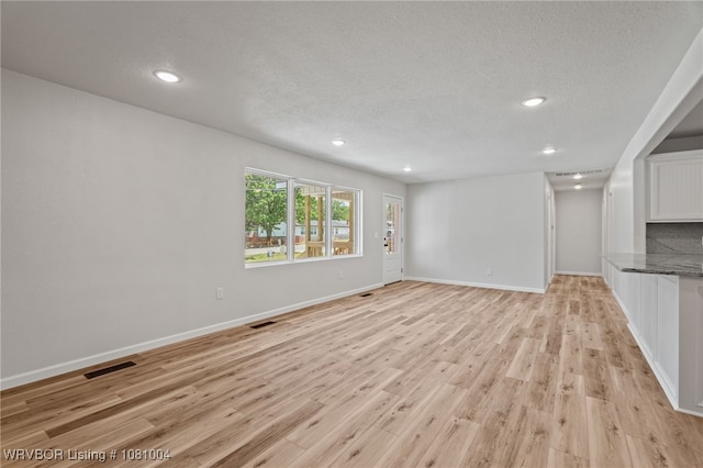 unfurnished living room featuring recessed lighting, light wood-style flooring, baseboards, and a textured ceiling