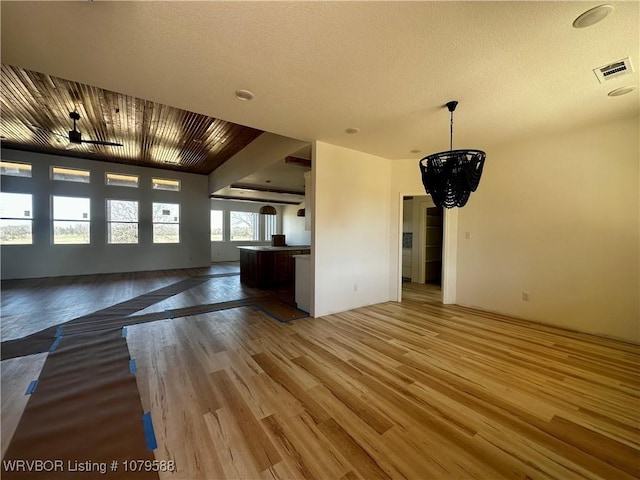 unfurnished living room with a chandelier, visible vents, a textured ceiling, and wood finished floors