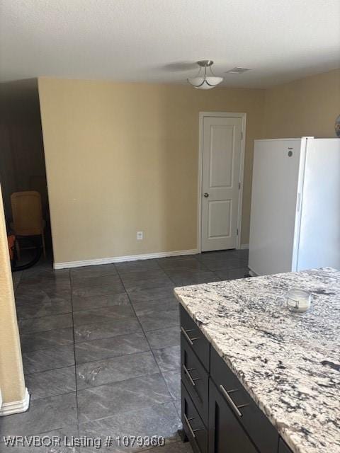 kitchen featuring visible vents, baseboards, light stone counters, and freestanding refrigerator