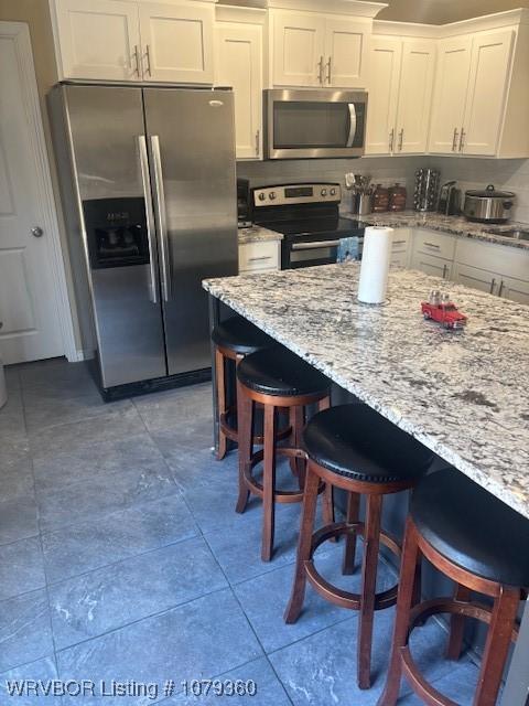 kitchen with light tile patterned floors, a breakfast bar, white cabinetry, appliances with stainless steel finishes, and light stone countertops