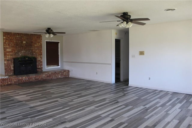 unfurnished living room featuring a textured ceiling, visible vents, baseboards, wood finished floors, and a ceiling fan