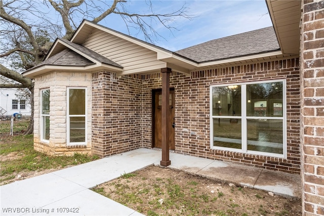 view of exterior entry with brick siding and a shingled roof