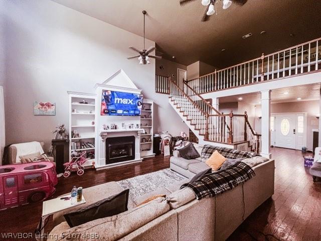 living room with wood-type flooring, ornate columns, ceiling fan, and a high ceiling