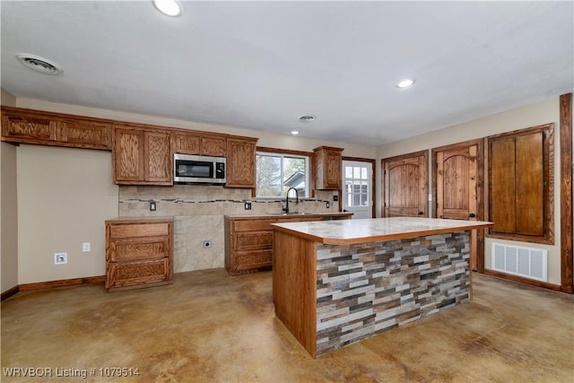 kitchen with concrete floors, stainless steel microwave, visible vents, and brown cabinetry