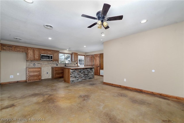 kitchen with stainless steel microwave, a kitchen island, concrete floors, baseboards, and brown cabinets