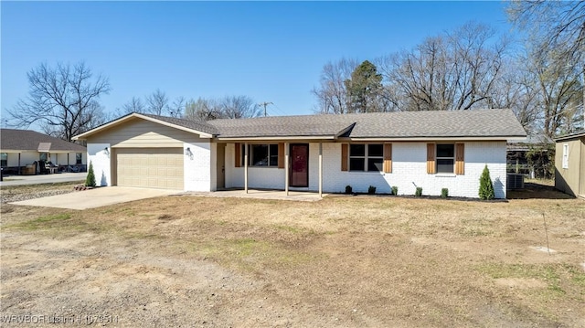 single story home with driveway, a porch, an attached garage, brick siding, and central AC unit