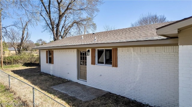 doorway to property featuring fence, brick siding, and a shingled roof