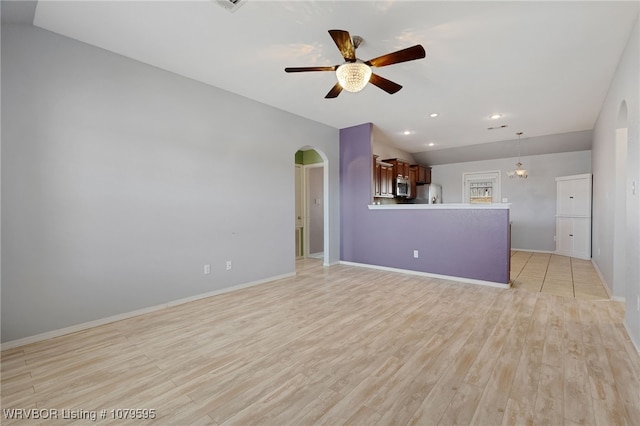 unfurnished living room featuring ceiling fan, vaulted ceiling, arched walkways, and light wood-type flooring