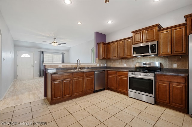 kitchen with a sink, ceiling fan, stainless steel appliances, dark countertops, and backsplash