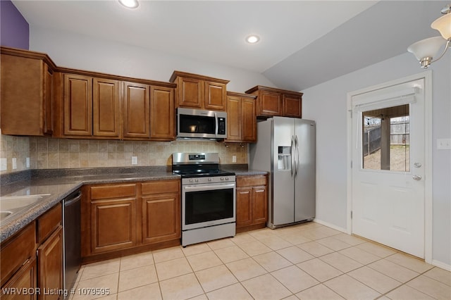 kitchen featuring decorative backsplash, vaulted ceiling, appliances with stainless steel finishes, dark countertops, and brown cabinets