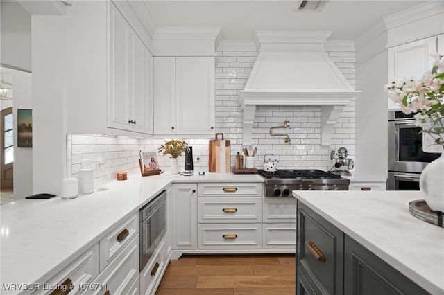 8801 Rombauer Pt, Fort Smith, AR 72916 - kitchen featuring ornamental molding, wood finished floors, white cabinetry, stainless steel appliances, and custom exhaust hood