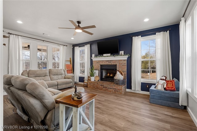 living room featuring ceiling fan, wood-type flooring, and a brick fireplace