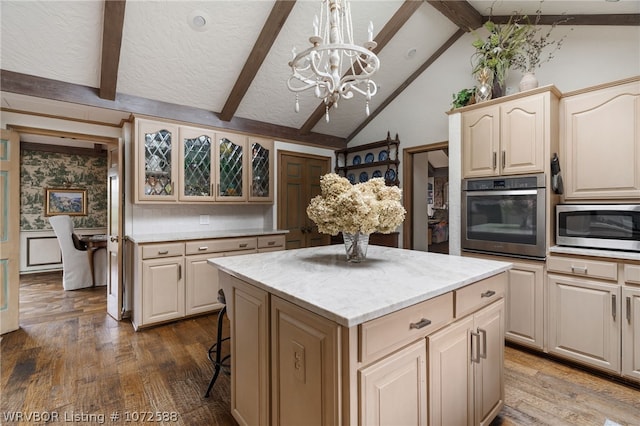 kitchen with a center island, vaulted ceiling with beams, appliances with stainless steel finishes, decorative light fixtures, and dark hardwood / wood-style flooring