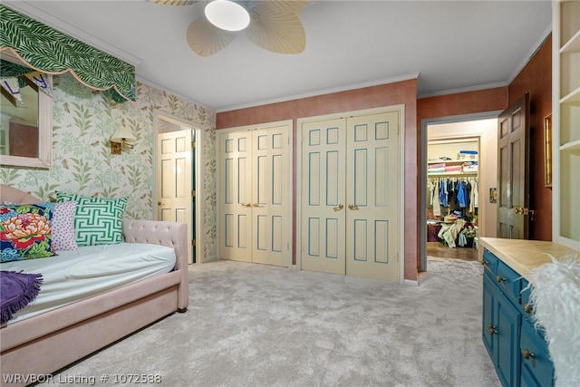 carpeted bedroom with ceiling fan, crown molding, and two closets