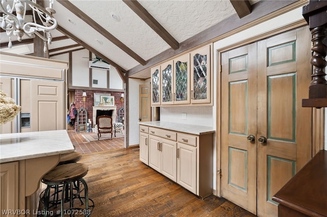 kitchen with a kitchen breakfast bar, vaulted ceiling with beams, dark hardwood / wood-style floors, a textured ceiling, and light stone counters