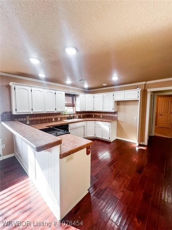 kitchen with kitchen peninsula, tile counters, dark hardwood / wood-style floors, tasteful backsplash, and white cabinets