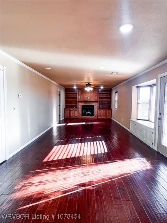 unfurnished living room with ceiling fan, dark wood-type flooring, built in features, and ornamental molding