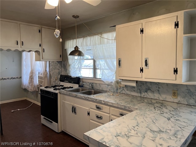 kitchen with white gas range oven, decorative light fixtures, white cabinetry, and sink