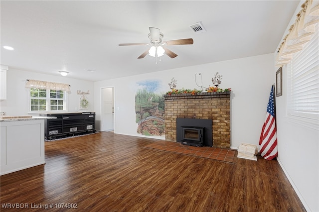 living room with ceiling fan, a wood stove, and dark wood-type flooring