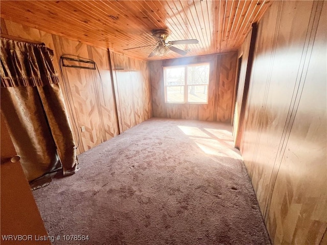 carpeted empty room with wood ceiling, wooden walls, and ceiling fan