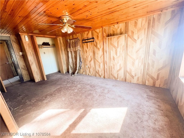 unfurnished bedroom featuring ceiling fan, wooden walls, carpet floors, wooden ceiling, and a closet