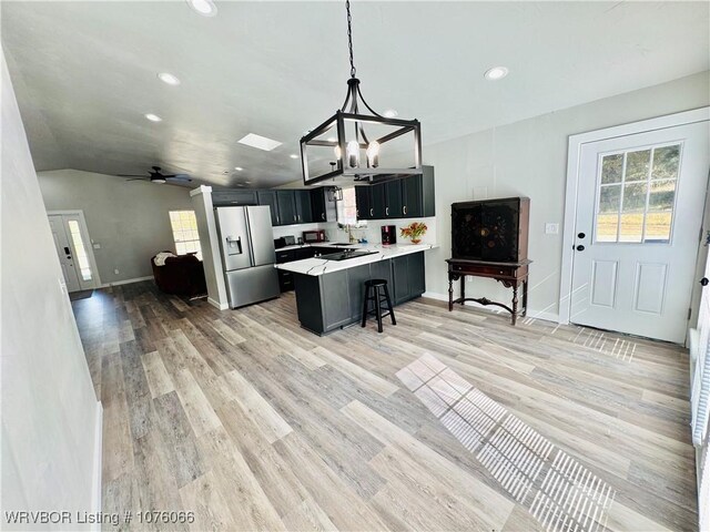 kitchen with a breakfast bar, ceiling fan with notable chandelier, vaulted ceiling, decorative light fixtures, and stainless steel fridge with ice dispenser