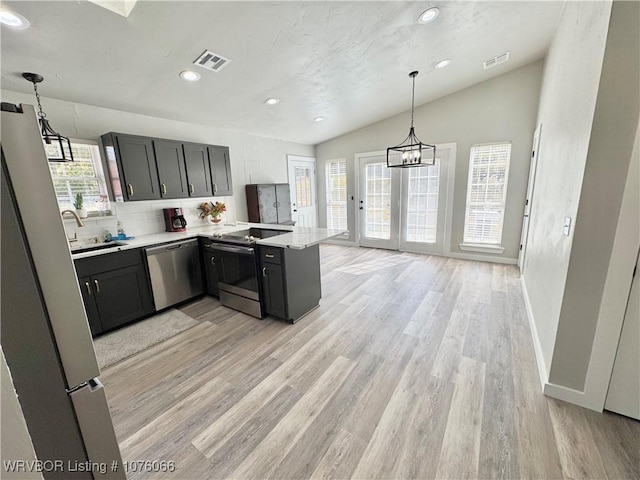 kitchen featuring light wood-type flooring, backsplash, stainless steel appliances, decorative light fixtures, and lofted ceiling