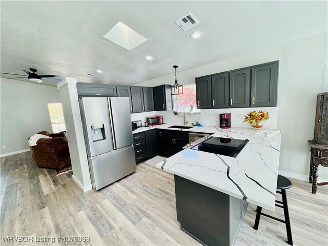 kitchen with a skylight, light stone countertops, decorative light fixtures, a breakfast bar, and appliances with stainless steel finishes