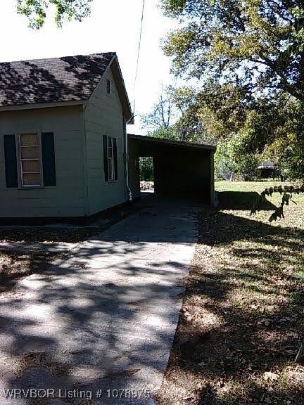 view of side of property with driveway, an attached carport, and roof with shingles