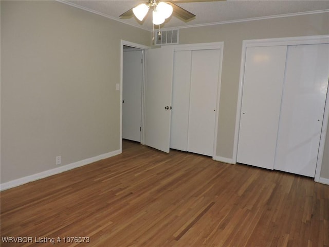 unfurnished bedroom with hardwood / wood-style floors, ceiling fan, ornamental molding, and multiple closets