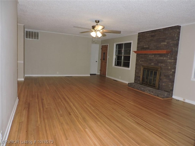 unfurnished living room featuring ceiling fan, hardwood / wood-style flooring, a textured ceiling, and a brick fireplace