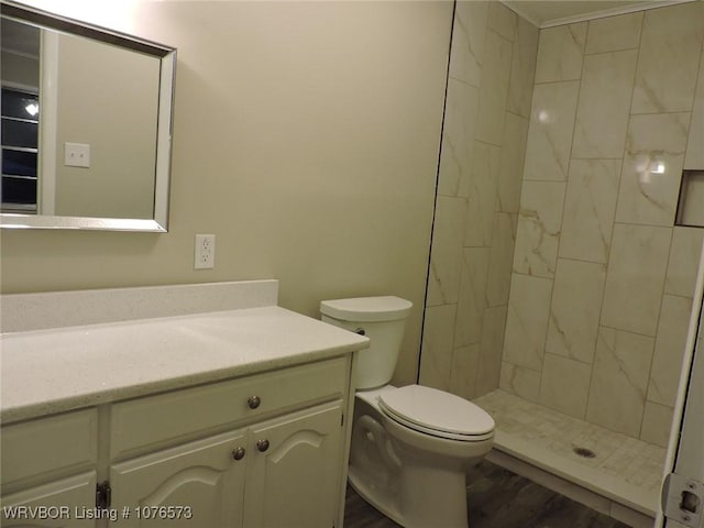 bathroom with toilet, hardwood / wood-style floors, vanity, and tiled shower