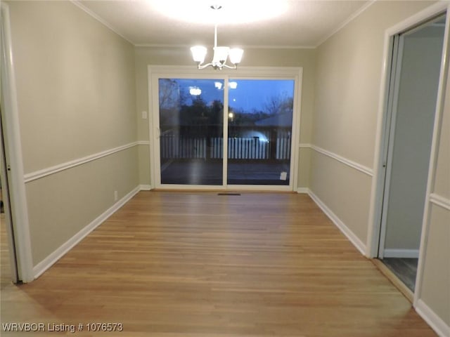 unfurnished dining area featuring wood-type flooring, an inviting chandelier, and crown molding