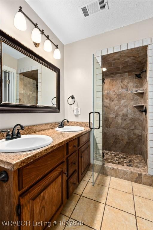 bathroom with tile patterned floors, vanity, a shower with door, and a textured ceiling