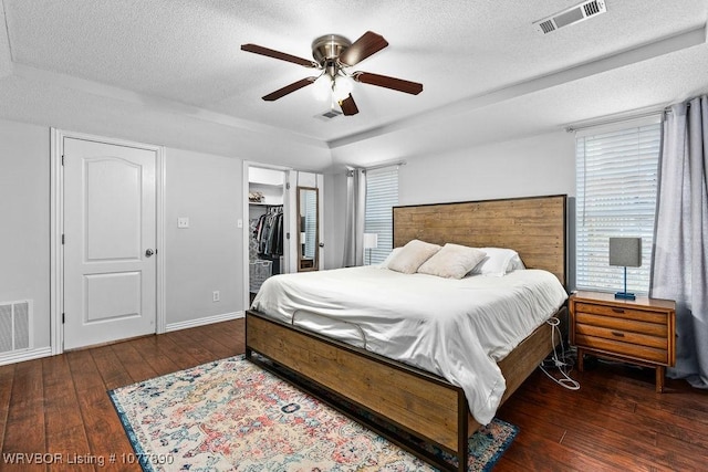 bedroom with ceiling fan, dark hardwood / wood-style flooring, a spacious closet, and a textured ceiling