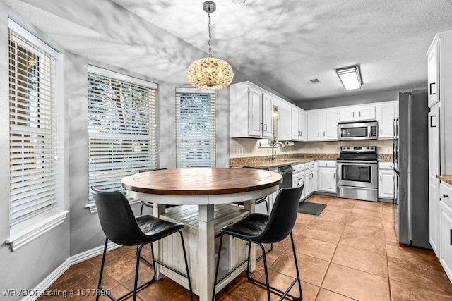 kitchen featuring pendant lighting, sink, light tile patterned floors, white cabinetry, and stainless steel appliances