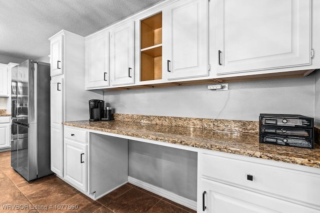 kitchen with stainless steel refrigerator, dark tile patterned floors, dark stone counters, a textured ceiling, and white cabinets