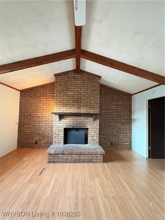 unfurnished living room with lofted ceiling with beams, light hardwood / wood-style floors, a brick fireplace, and brick wall