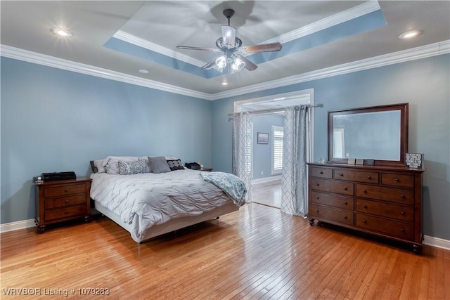 bedroom featuring baseboards, a raised ceiling, hardwood / wood-style flooring, ceiling fan, and ornamental molding