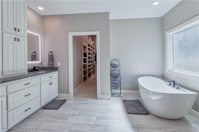 bathroom with a freestanding tub, recessed lighting, vanity, baseboards, and a spacious closet