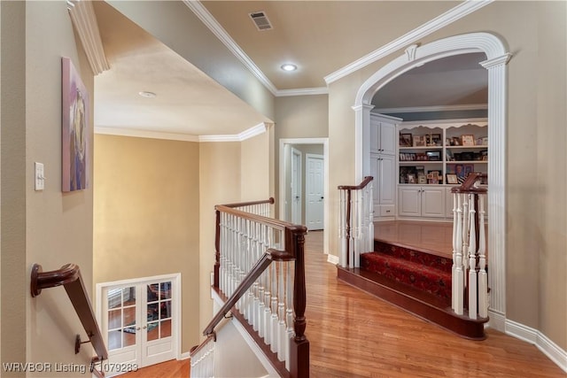 hallway with light wood-style flooring, an upstairs landing, visible vents, baseboards, and ornamental molding